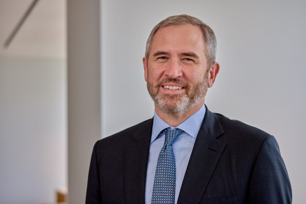 Happy man in a suit and tie stands before a simple, light backdrop.